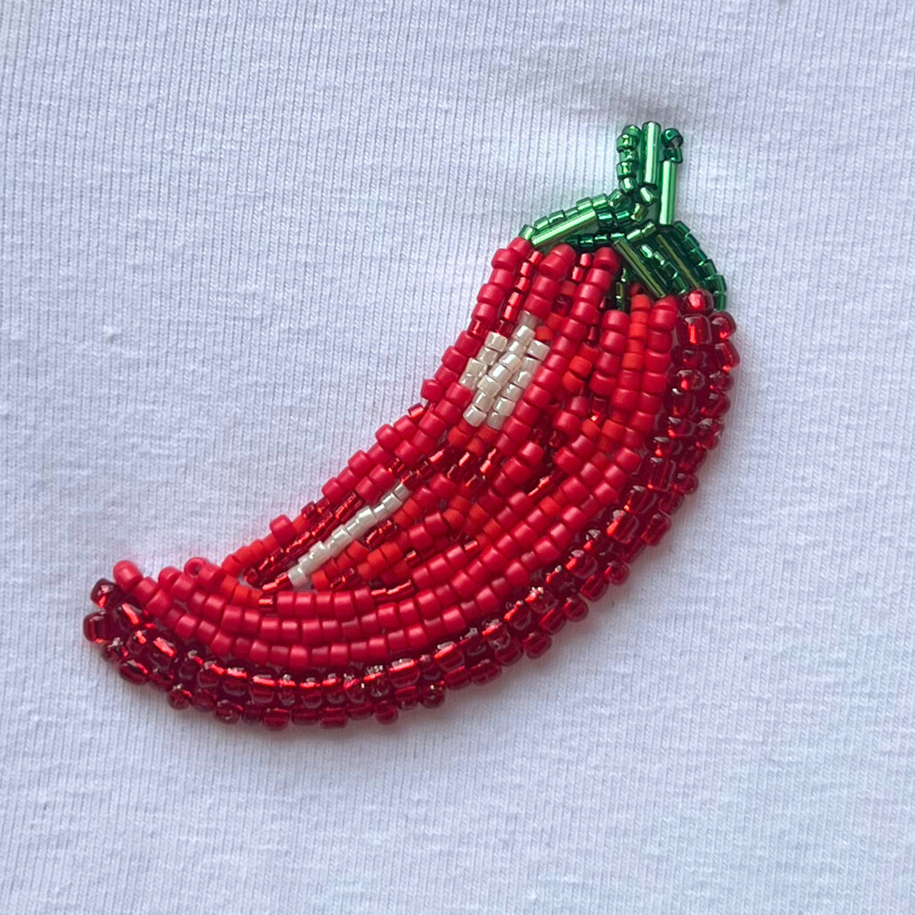 Beaded embroidery red chili pepper on a blue lightfabric background