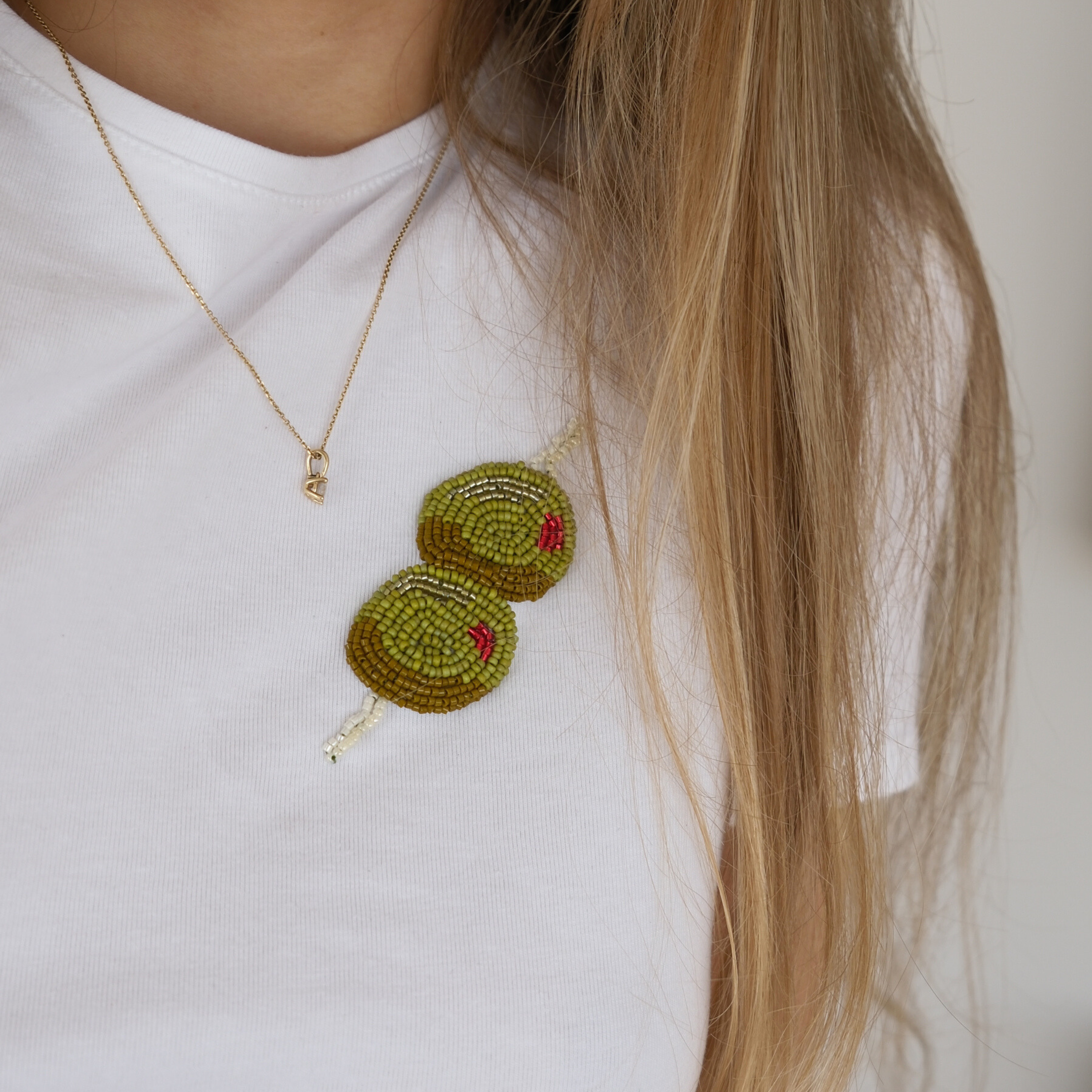Close-up of woman wearing white t-shirt with DIY olive beaded embroidery design made from green, gold, and red Miyuki seed beads.