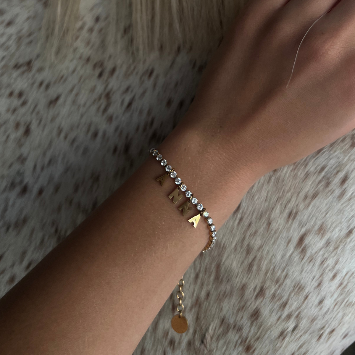 Hand wearing a DIY tennis bracelet with gold-plated letter charms spelling ANNA and zirconia stones on a delicate chain.