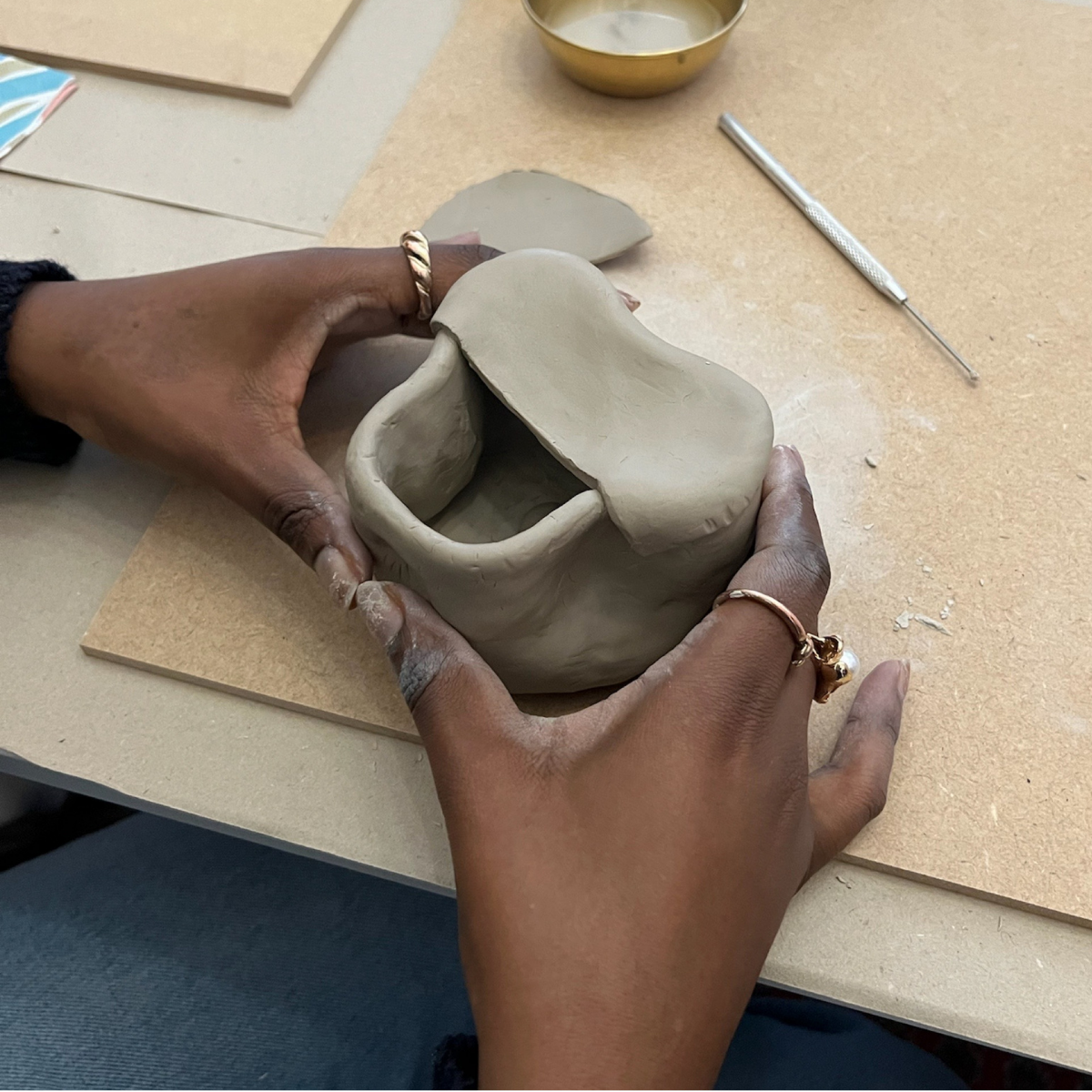 Person holding a clay pot on a pottery wheel with tools and materials in the background