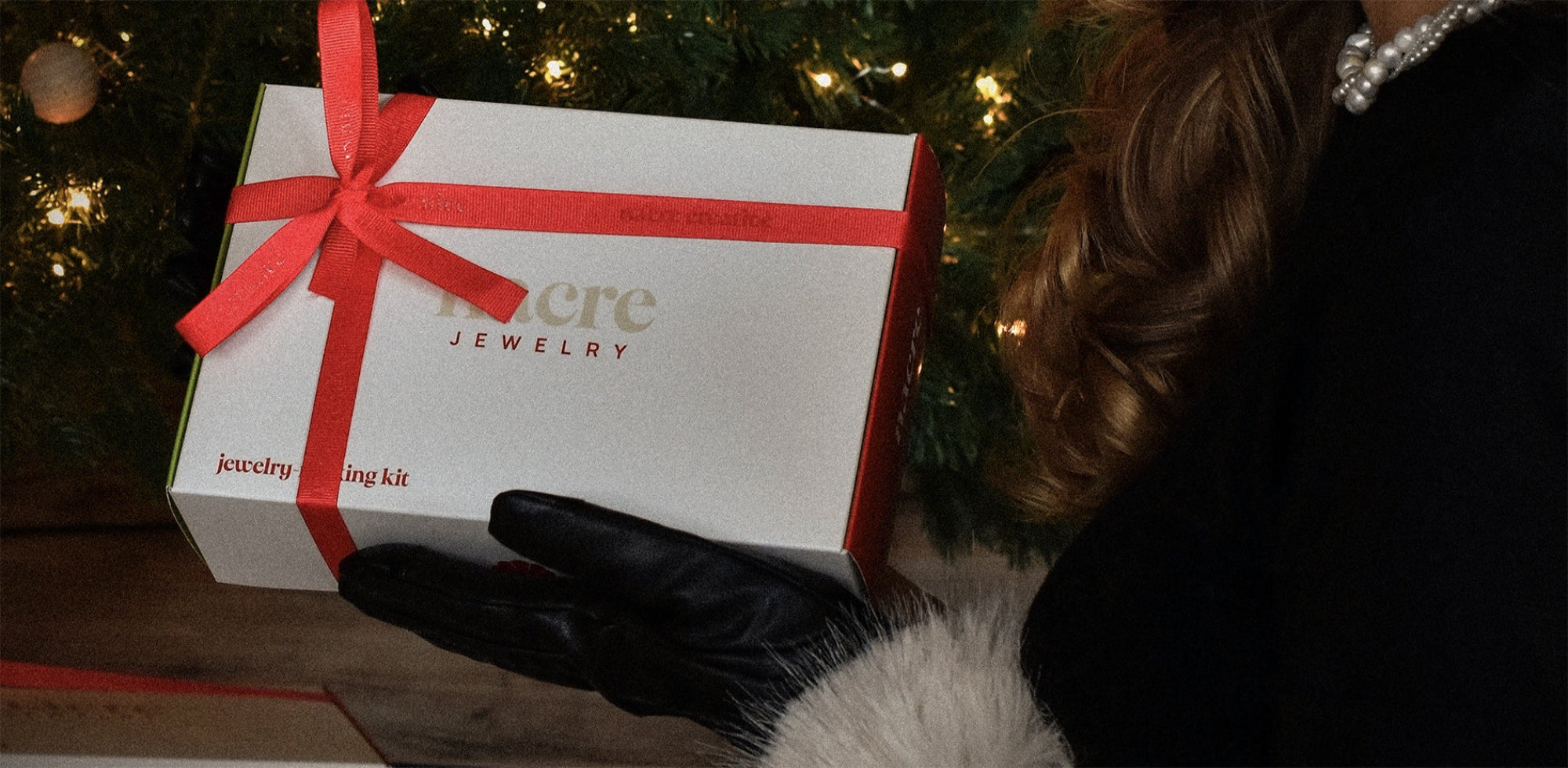 Jewelry making gift box held by a person with a fur-lined coat against a Christmas tree background