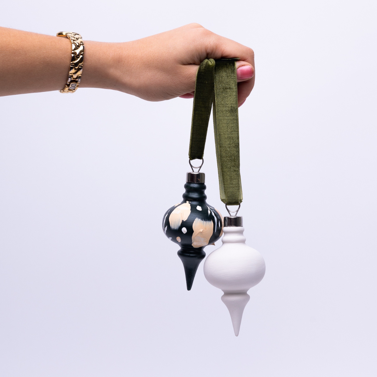 Hand holding two decorative ornaments with a green strap against a white background