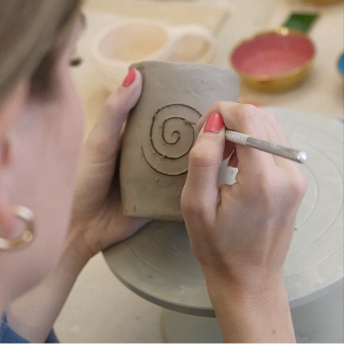 Person decorating a ceramic pot with a spiral design using a tool.