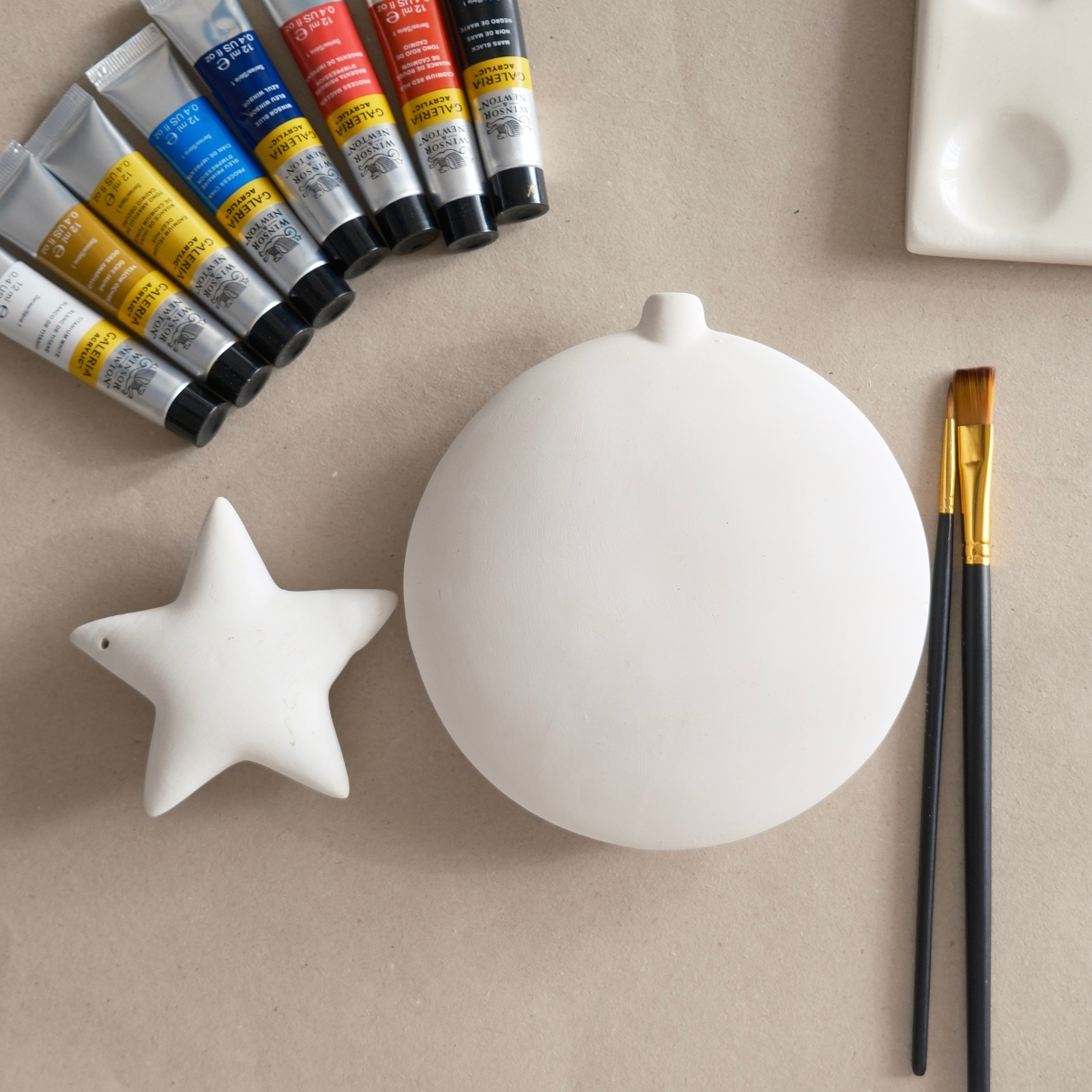 White ceramic star and sphere with paint tubes and a brush on a beige surface