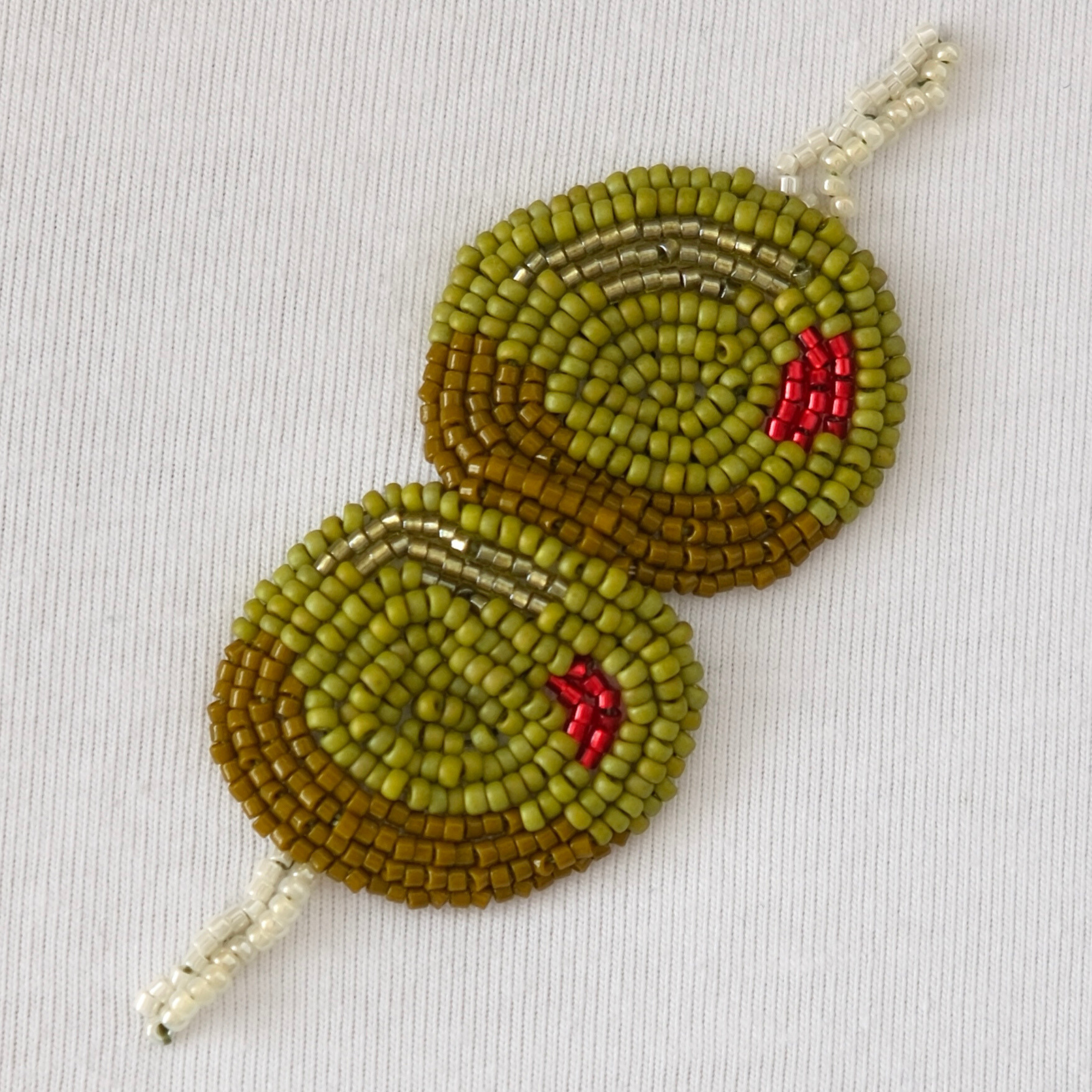 Close-up of handmade olive beaded embroidery design with green, gold, and red Miyuki seed beads on white fabric.